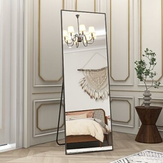 Floor mirror reflecting a cozy bedroom with chandelier and wall decor.