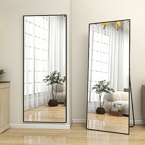 Two large floor mirrors reflecting a room with a plant and sheer curtains.