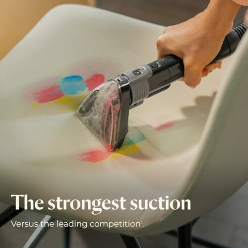 Hand using a vacuum cleaner on a stained chair.