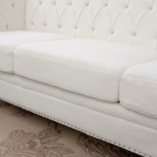 Close-up of a white upholstered sofa with button tufting.